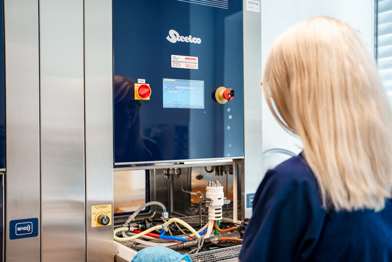 Eine Medizinische Fachangestellt reinigt die Untersuchungsgeräte an einer Desinfektionsmaschine.