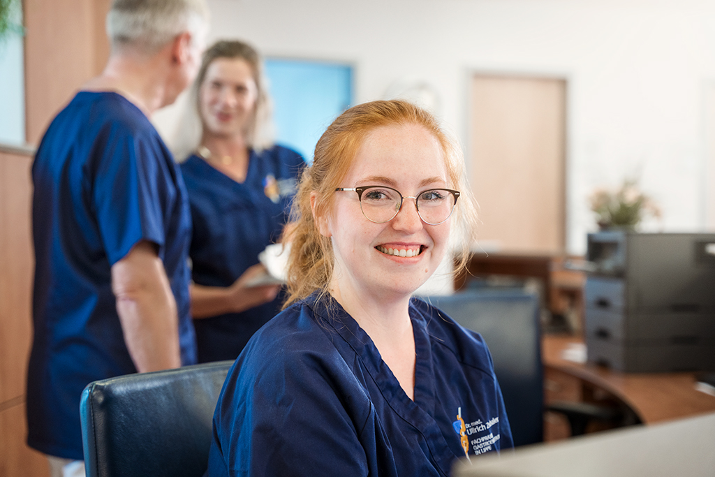 Eine lächelnde Arzthelferin sitzt am Empfangstresen